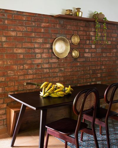 Dining table with cane chairs against exposed brick wall hung with brass plates