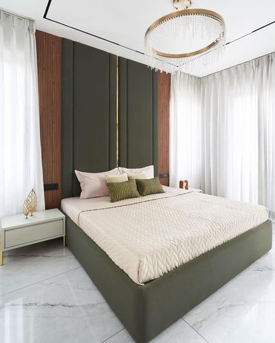Bedroom with tall olive green tufted headboard, wood slat panels, and crystal ring chandelier