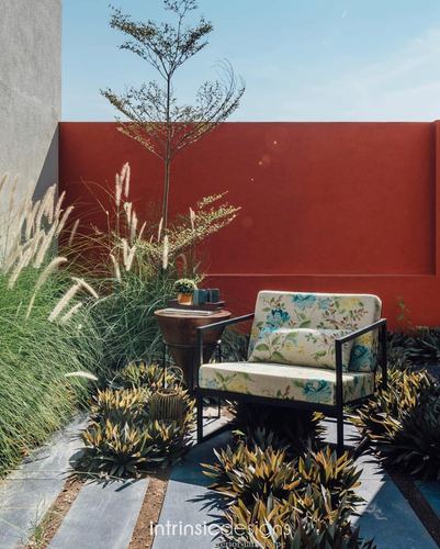 Outdoor seating nook with floral armchair against a red plastered wall and ornamental grasses