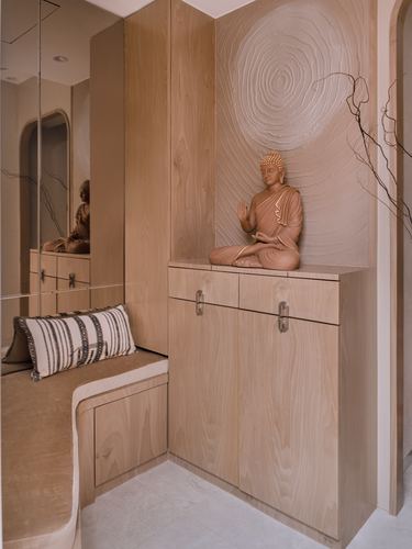 Wooden foyer cabinet with a seated buddha statue against a textured spiral wall panel