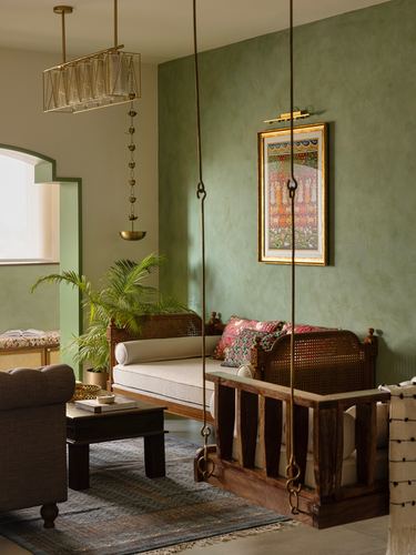 Green-walled living room with a wooden cane swing, framed art, and brass lamp