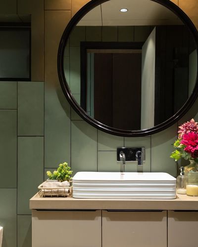 Sage green tiled bathroom vanity with round black mirror and white vessel sink