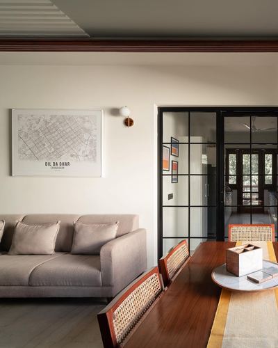 Living room with taupe sofa, framed city map, and black steel-glass partition leading to dining area