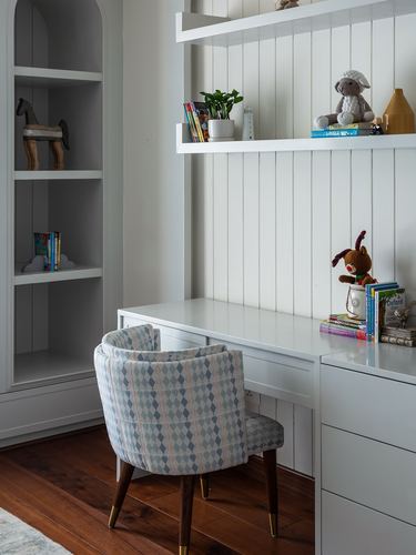 Child's study desk with patterned chair, panelled wall shelves, and arched built-in bookcase