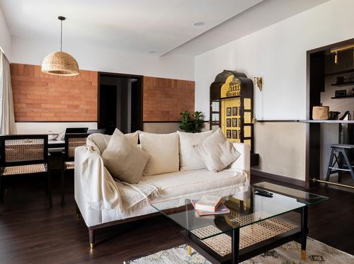 Living room with cream sofa, glass coffee table, brick accent wall and cane dining chairs