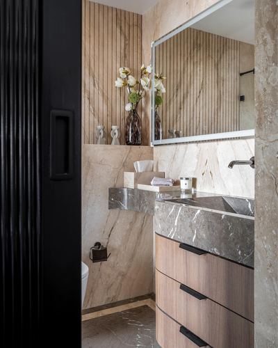 Bathroom vanity with curved wood drawers and grey stone counter, framed by fluted black door