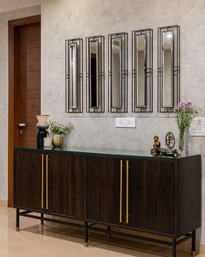 Fluted dark wood sideboard with brass handles beneath five vertical mirror panels in a foyer