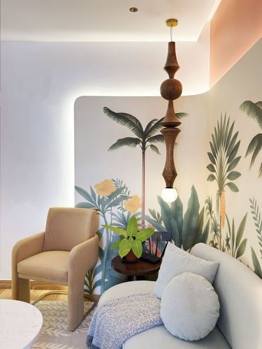 Curved wall niche with tropical mural, turned wood pendant light, beige armchair and pale blue sofa