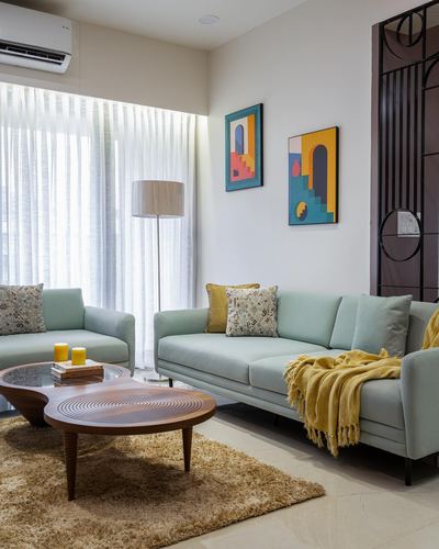 Sage green sofas around carved wood coffee tables with colorful art deco wall art and sheer curtains