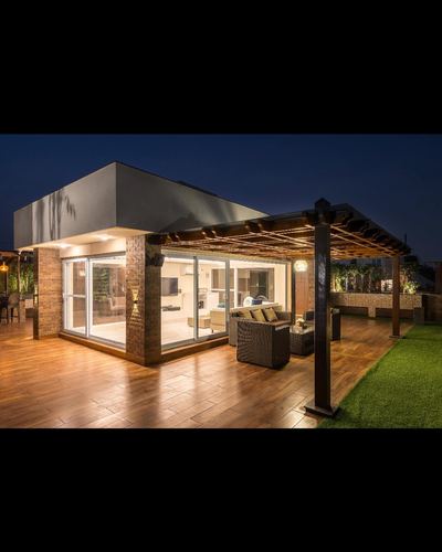Rooftop terrace at night with pergola, wicker seating, wood deck and glass house