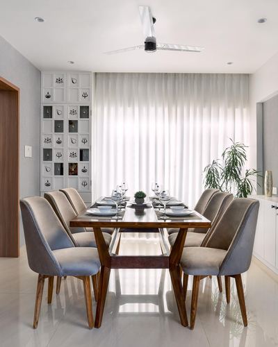 Dining room with wooden table, grey velvet chairs, sheer curtains, and decorative wall panel
