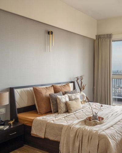 Bedroom with tufted headboard, layered cushions, brass sconce, and city view through window