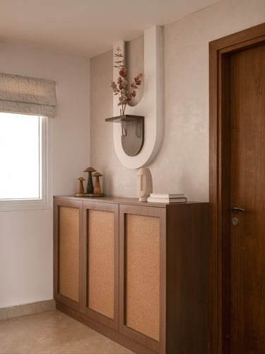 Foyer with cane-front wood cabinet, arched plaster niche, and wooden door beside a curtained window