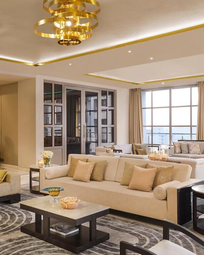 Beige living room with gold chandelier, cream sofas, patterned rug and floor-to-ceiling windows