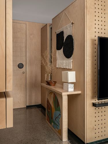 Plywood-clad foyer with arched painted console, textile wall hanging, terrazzo floor