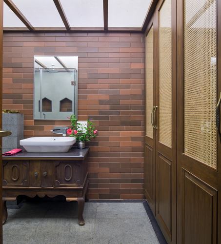 Bathroom with brick-tile wall, antique wood vanity, vessel sink, and cane-panelled wardrobe