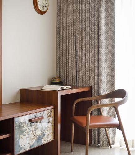 Wooden study desk and curved armchair beside patterned curtain and marble-fronted cabinet