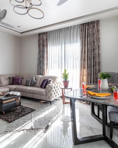 Living and dining area with tufted sofa, marble floor, and floor-to-ceiling patterned curtains