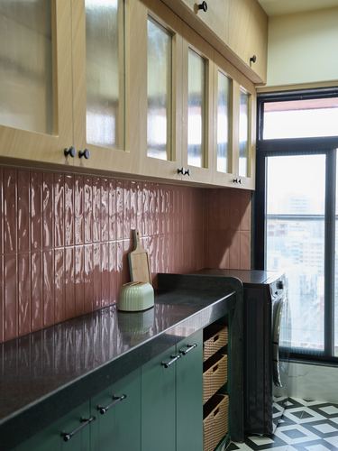Kitchen corner with terracotta ribbed tile backsplash, sage green cabinets, black countertop and glass window.