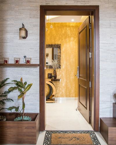Entry foyer with stone wall, open wood door, and view into gold-walled console alcove with starburst mirror