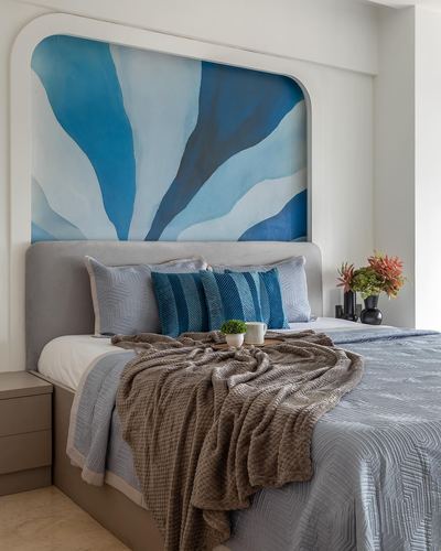 Bedroom with arched blue abstract mural above grey upholstered bed and knit throw