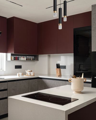 Modern kitchen with maroon overhead cabinets, white stone island, and black cylindrical pendant lights