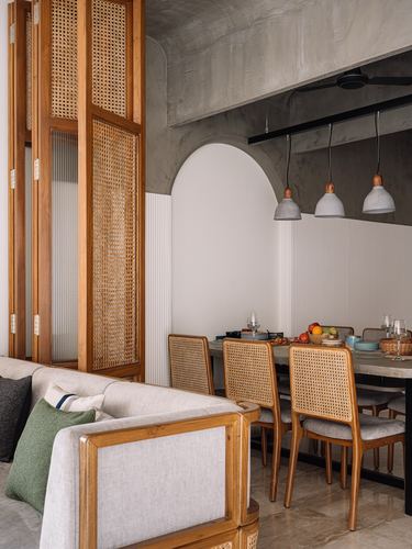 Dining area with cane chairs, arched niche, and concrete pendant lights beside a cane room divider
