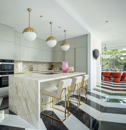 Kitchen with marble waterfall island, brass globe pendants, geometric marble floor, view to dining area