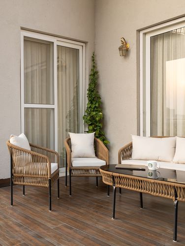 Balcony seating with woven armchairs, sofa, and glass coffee table beside a climbing plant