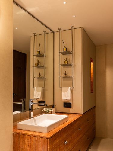 Bathroom with wood vanity, vessel sink, and suspended brass-figurine shelves against a mirrored wall