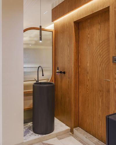 Ribbed dark pedestal sink in alcove beside carved wood door in Mumbai home