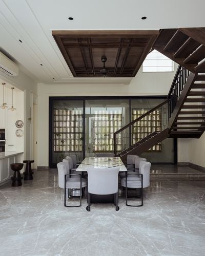 Marble-floored dining area beneath a wood-panelled ceiling drop, with staircase and slatted screen behind