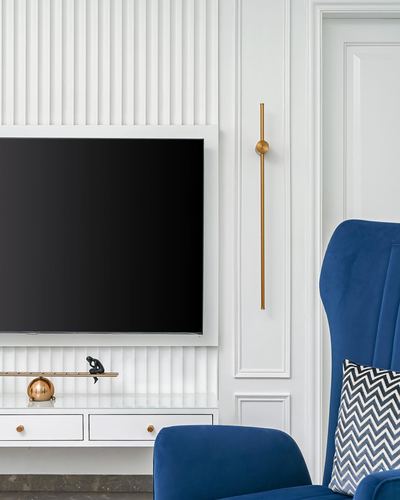 Fluted white wall with mounted TV, brass sconce, and navy velvet armchair with chevron cushion