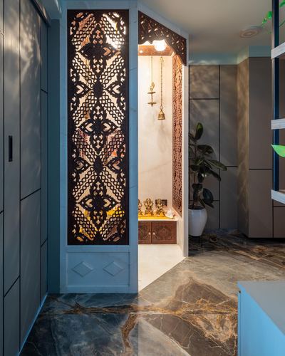 Carved wooden jali screen opens to a marble pooja niche with hanging brass bell and idols