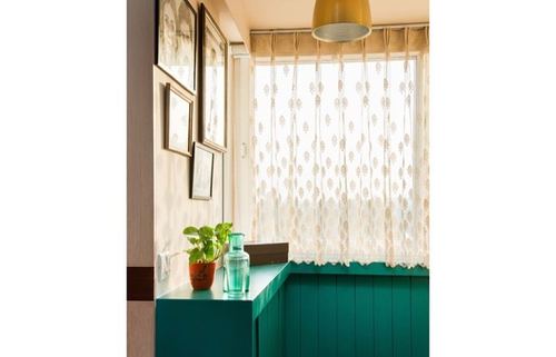 Teal-paneled corner with framed art, lace curtains and sunlit window in an apartment foyer
