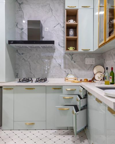 Mint green kitchen with marble-look backsplash, brass handles, and open drawer showing storage