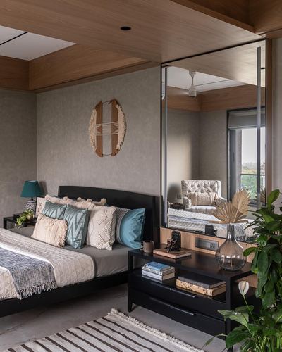 Bedroom with wood-clad ceiling, black bed frame, teal and cream pillows, and a large leaning mirror reflecting an armchair.