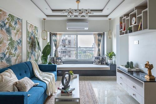 Living room with blue tufted sofa, window seat, tropical wall art and layered ceiling