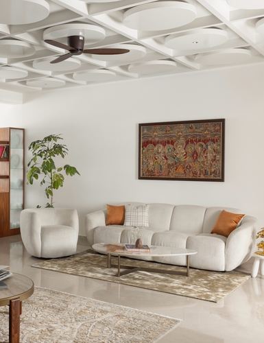 White living room with curved boucle sofa, framed traditional textile art, and coffered ceiling