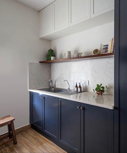 Galley kitchen with navy cabinets, white stone counter and backsplash, wood open shelf above