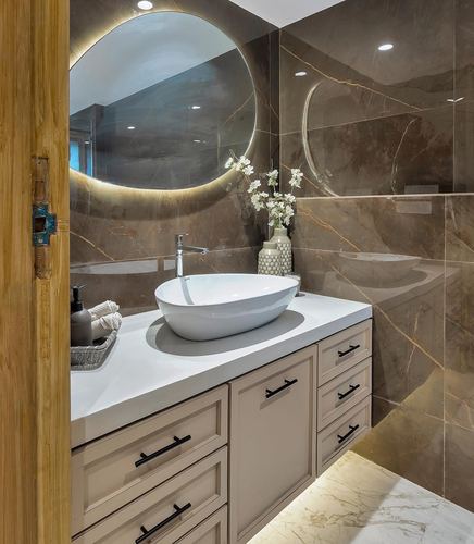 Bathroom vanity with oval vessel sink, backlit round mirror, and beige cabinetry against marbled stone walls
