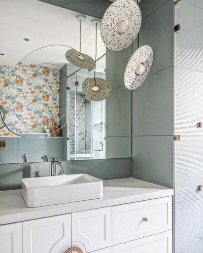 Sage green bathroom vanity with terrazzo disc pendant lights and floral wallpaper reflected in mirror