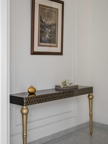Console table with brass diamond inlay under a framed vintage print on paneled wall