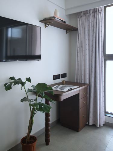 Study nook with wall-mounted tv, wooden shelf, turned-leg desk, monstera plant, and patterned curtain by window
