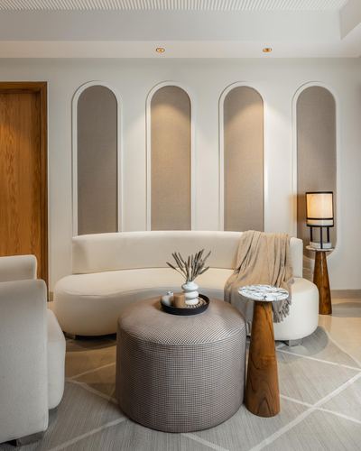Curved white sofa before arched fabric niches with a conical wood side table and round ottoman