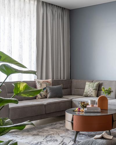 Grey corner sofa with patterned cushions beside sheer curtains and a round marble-top coffee table