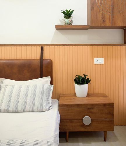 Bedroom corner with tan leather headboard, ribbed terracotta wall panel, and wooden nightstand with plant