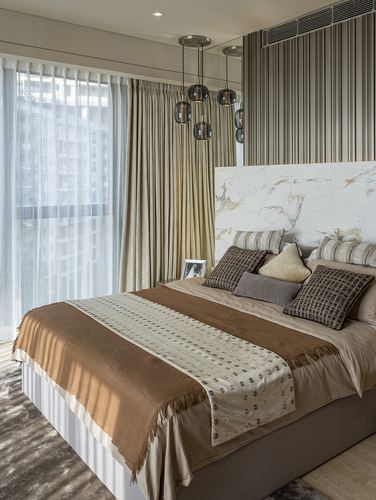 Bedroom with marble headboard, layered brown and beige bedding, sheer curtains, and cluster pendant lights