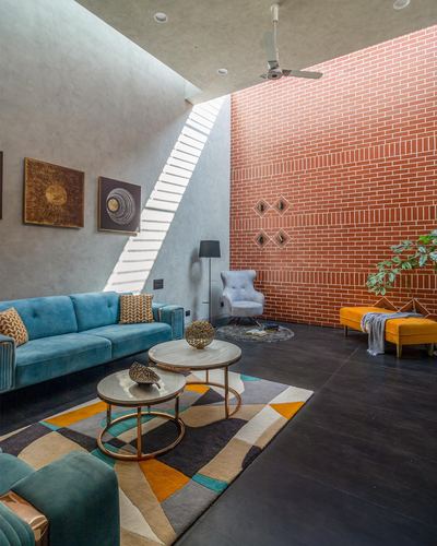 Double-height living room with exposed brick wall, teal velvet sofa, and geometric rug lit by a skylight.