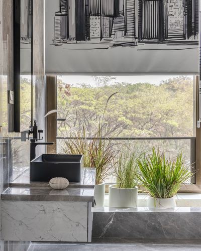 Black square vessel sink on veined stone counter beside window with potted grasses and tree view